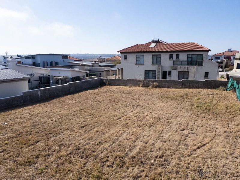 A vacant residential plot of land enclosed by boundary walls, situated within a developed suburban neighborhood.