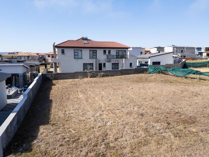 An aerial view of a vacant residential plot enclosed by boundary walls in a developed suburban neighborhood.