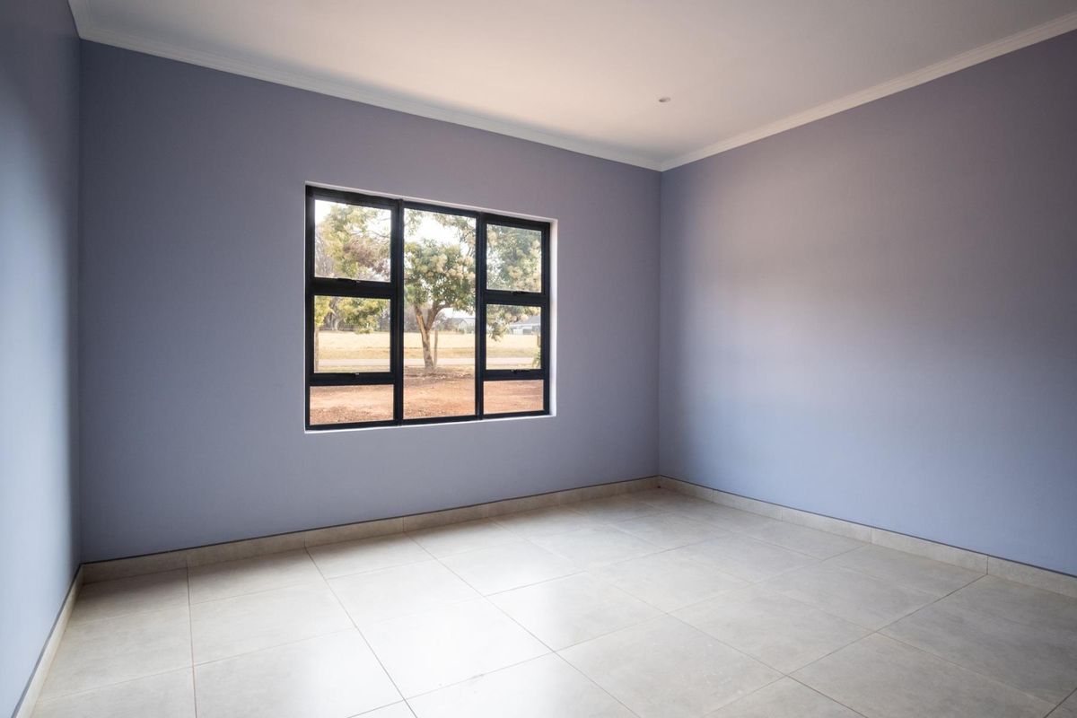 A clean, empty bedroom featuring neutral tiled flooring, soft grey walls, and a modern black aluminium window frame.