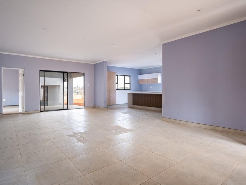 Spacious open-plan living and kitchen area featuring neutral tiled flooring, recessed lighting, and direct access to an outdoor patio through sliding glass doors.