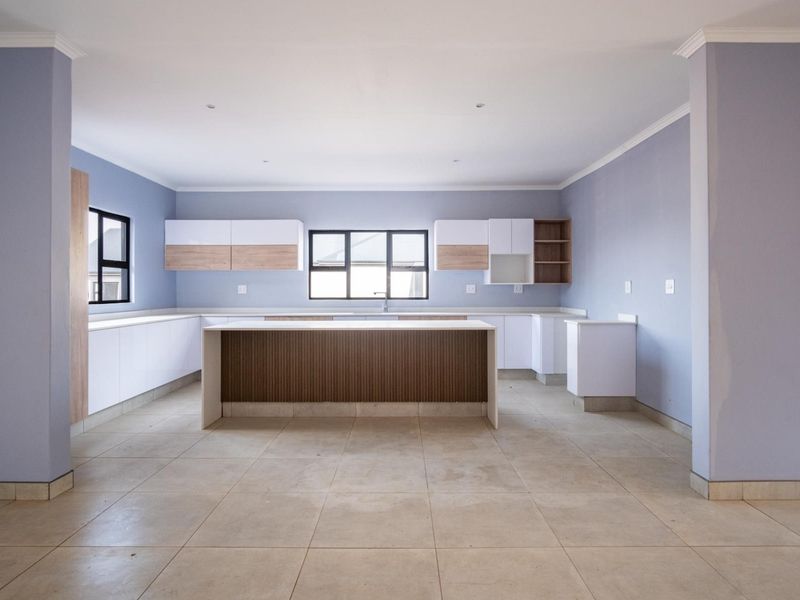 A spacious, modern kitchen featuring a central island, ample built-in cabinetry, and neutral tiled flooring, presented in a clean, empty state.