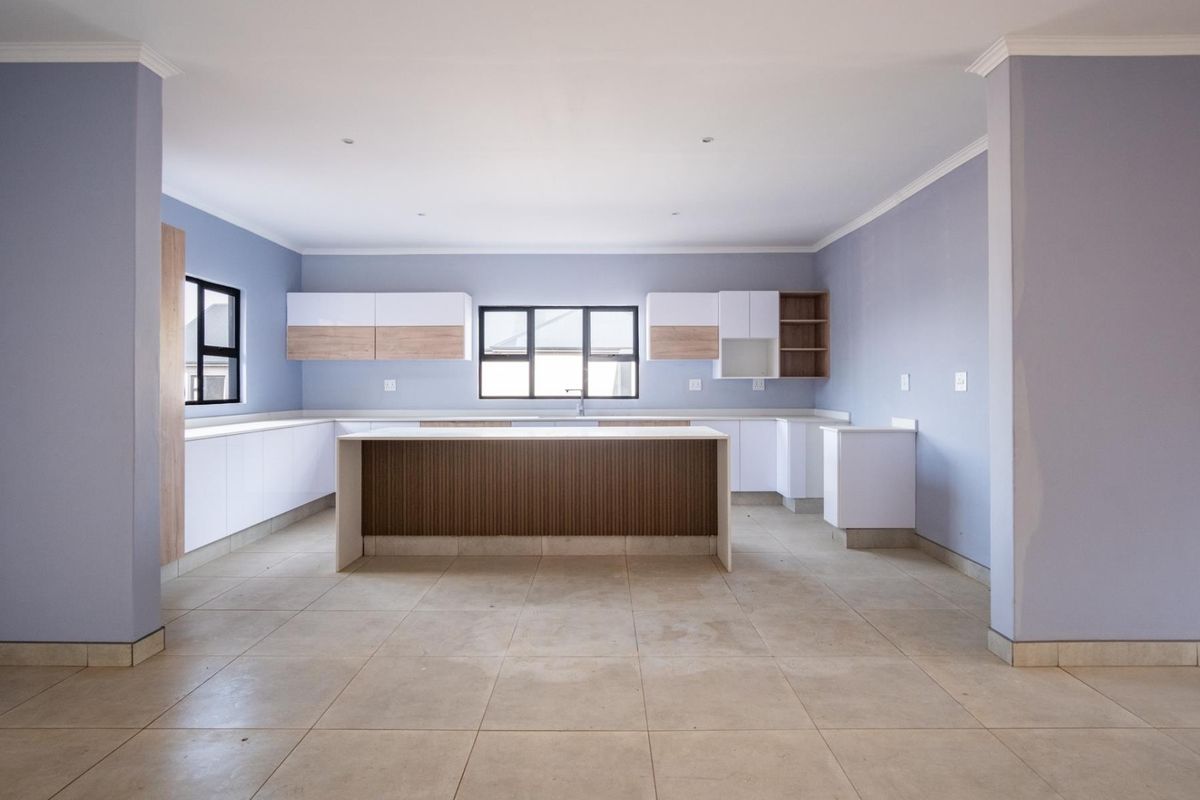A spacious, modern kitchen featuring a central island, ample built-in cabinetry, and neutral tiled flooring, presented in a clean, empty state.