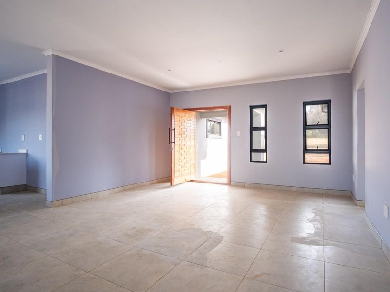 Spacious open-plan living area featuring neutral walls, tiled flooring, and direct access to the exterior through a solid wood front door.