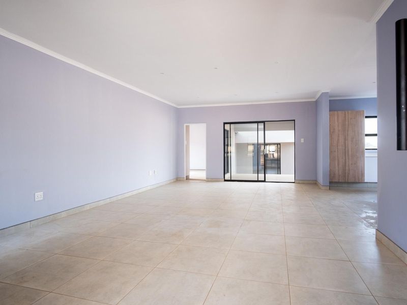 A spacious, empty living area featuring neutral tiled flooring, light-colored walls, and a modern sliding glass door leading to an adjacent space.
