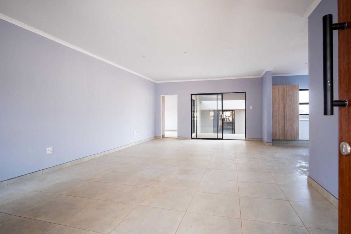 A spacious, empty living area featuring neutral tiled flooring, light-colored walls, and a modern sliding glass door leading to an adjacent space.
