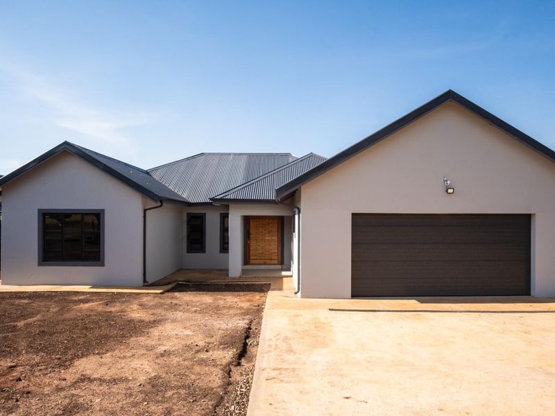 Front elevation of a modern townhouse featuring a double garage, timber entrance door, and corrugated metal roof with an unfinished garden area.
