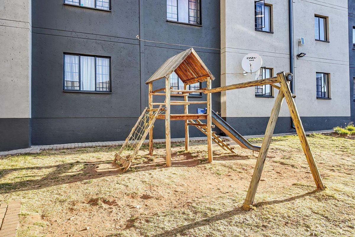 Rear exterior view of the apartment building featuring a communal garden area with a wooden playground structure and paved pathways.