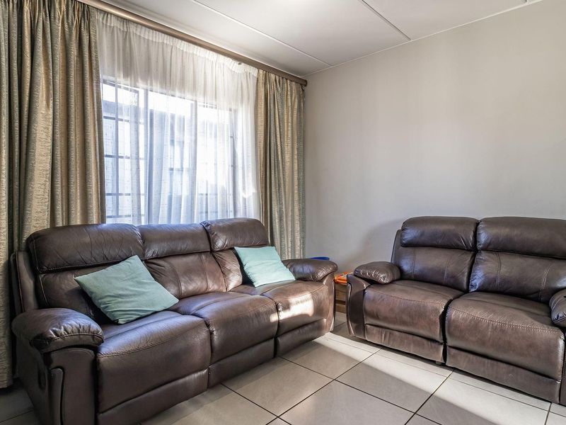 A living room featuring neutral tiled flooring and large windows with installed curtain tracks, providing a functional and well-lit space.