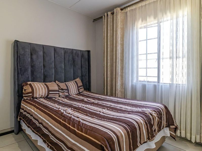 A well-maintained bedroom featuring tiled flooring and a window with security bars, providing natural light and a neutral backdrop.