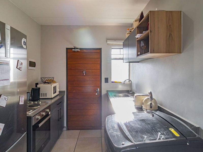 Compact kitchen featuring built-in oven, hob, stainless steel sink, and ample cabinetry, finished with tiled flooring and a solid wood entrance door.