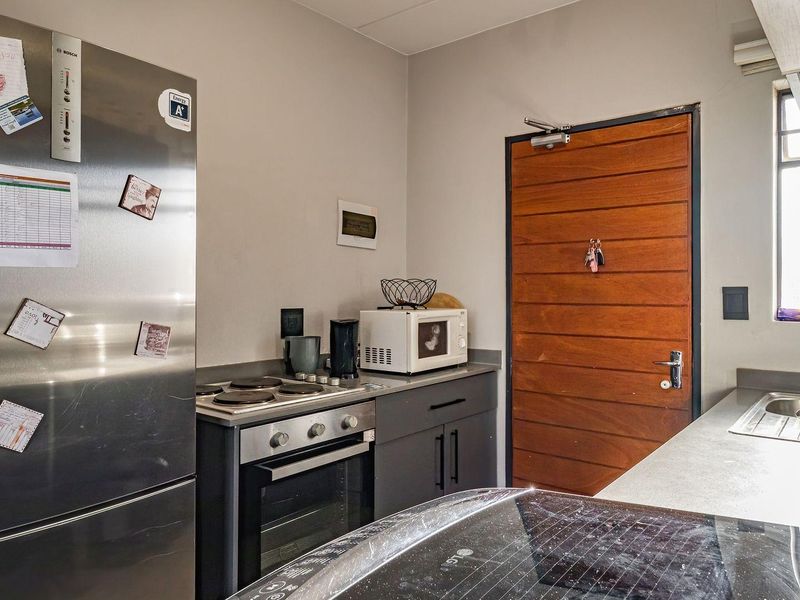 A functional kitchen featuring dark cabinetry, stone countertops, a built-in oven with electric hob, and a stainless steel sink with a timber entrance door.