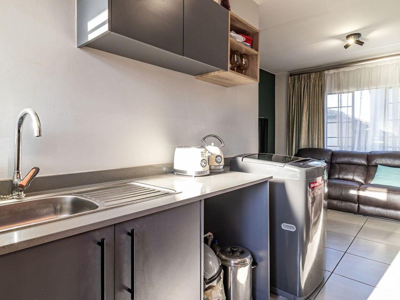 Open plan living area featuring a modern kitchenette with grey cabinetry, stone countertops, stainless steel sink, and tiled flooring throughout.