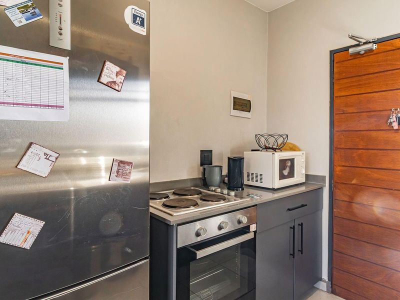 Compact kitchen area featuring built-in oven, electric hob, modern grey cabinetry, and a solid wood entrance door.