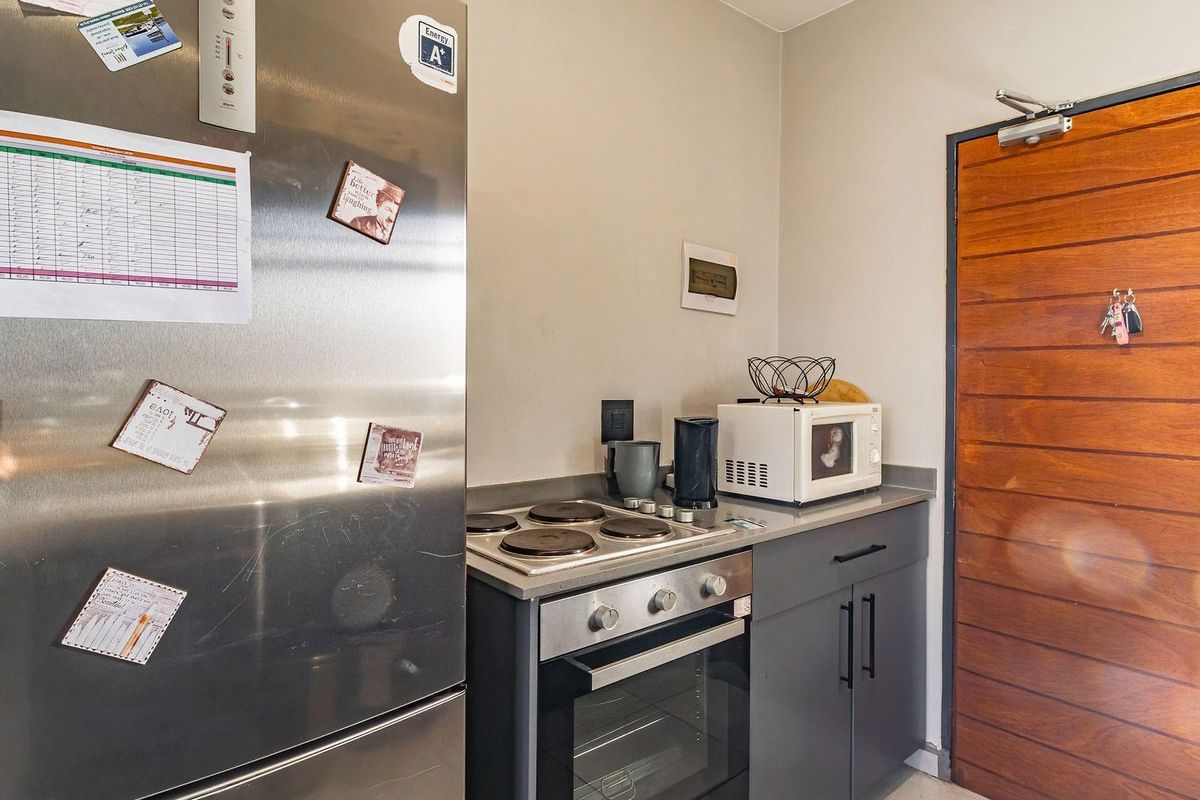 Compact kitchen area featuring built-in oven, electric hob, modern grey cabinetry, and a solid wood entrance door.
