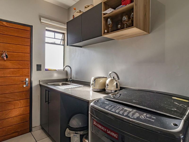 A functional laundry area featuring built-in cabinetry, a stainless steel sink, and tiled flooring, providing a practical space for household utility tasks.