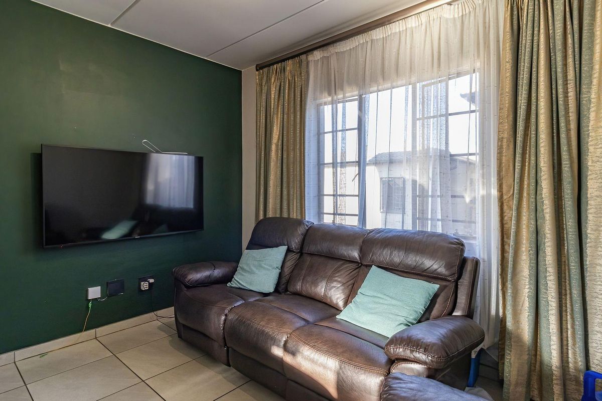 A living room featuring tiled flooring and a dark green accent wall, providing a functional space with natural light from the window.