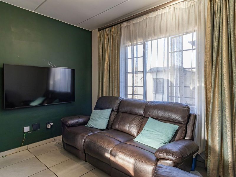A living room featuring tiled flooring and a dark green accent wall, providing a functional space with natural light from the window.