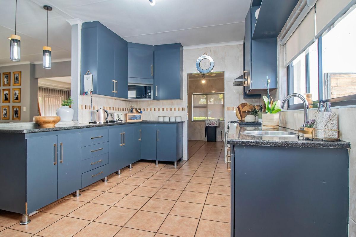 Modern kitchen featuring dark blue cabinetry, granite countertops, tiled flooring, and a functional layout with an adjacent scullery area.