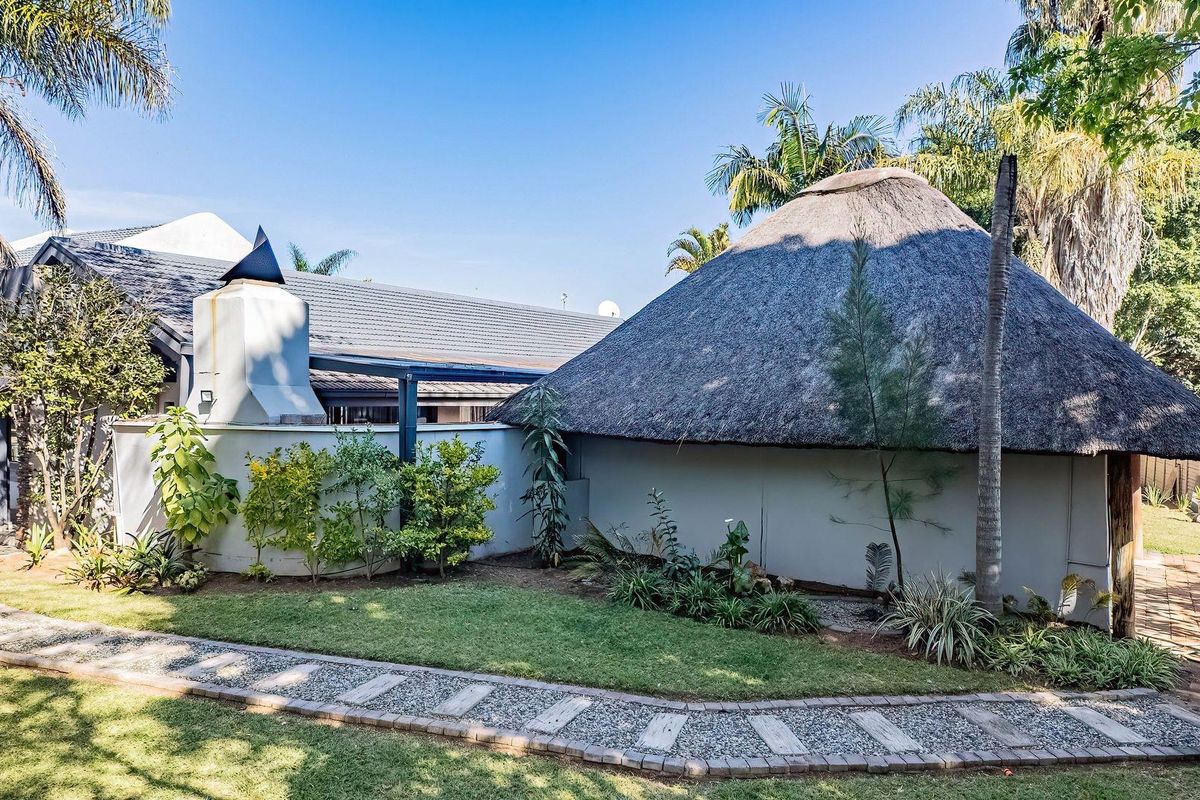 A well-maintained rear garden area featuring a unique thatched-roof structure, an outdoor fireplace, and a paved walkway set within a landscaped yard.