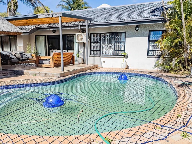 Rear exterior view featuring a swimming pool with safety net, covered patio area, and paved surroundings.