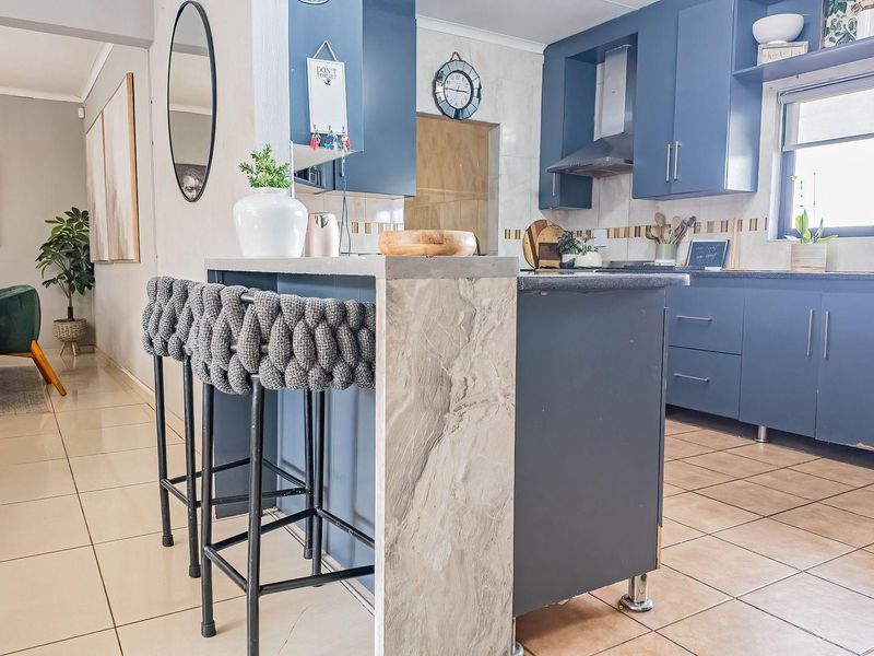 Modern open-plan kitchen featuring blue cabinetry, a stone-topped island, and tiled flooring, seamlessly connecting to the adjacent dining area.