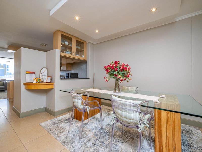 An open-plan dining area featuring tiled flooring, recessed ceiling lighting, and a convenient pass-through window connecting to the kitchen space.