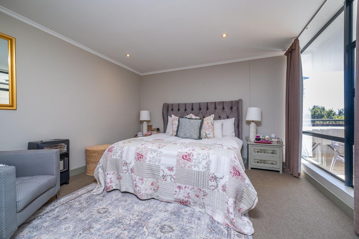 A well-maintained bedroom featuring neutral wall tones, carpeted flooring, recessed lighting, and direct access to an outdoor balcony through a large sliding glass door.