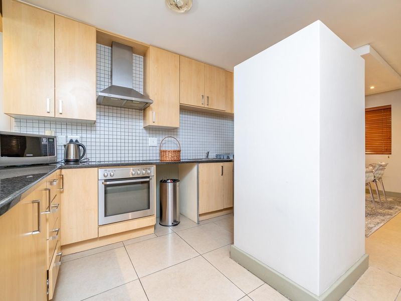 A functional kitchen featuring light wood cabinetry, a tiled backsplash, stainless steel extractor fan, and built-in oven, with tiled flooring throughout.
