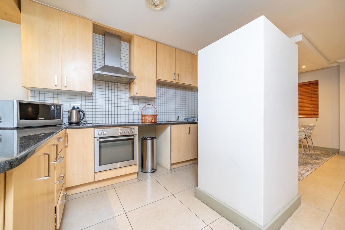 A functional kitchen featuring light wood cabinetry, a tiled backsplash, stainless steel extractor fan, and built-in oven, with tiled flooring throughout.
