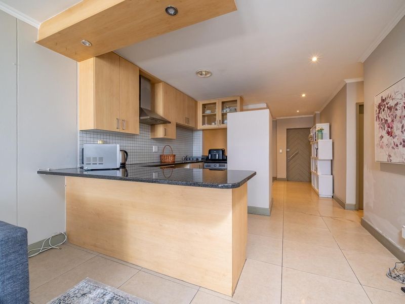 Open-plan kitchen featuring light wood cabinetry, granite countertops, a breakfast bar, and tiled flooring, seamlessly flowing into the entrance area.