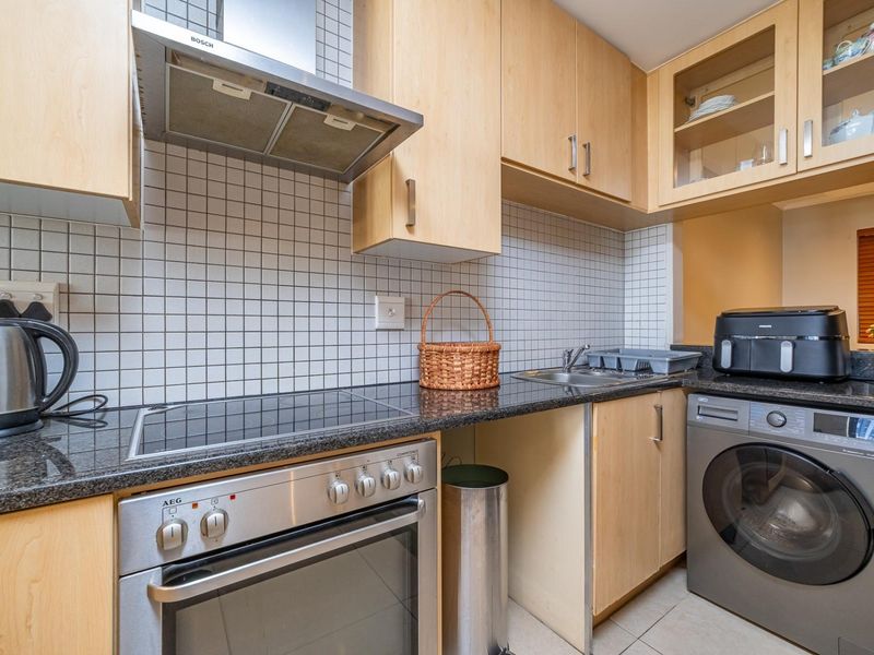 Compact kitchen featuring light wood cabinetry, granite countertops, tiled backsplash, and integrated stainless steel appliances including an oven and extractor fan.