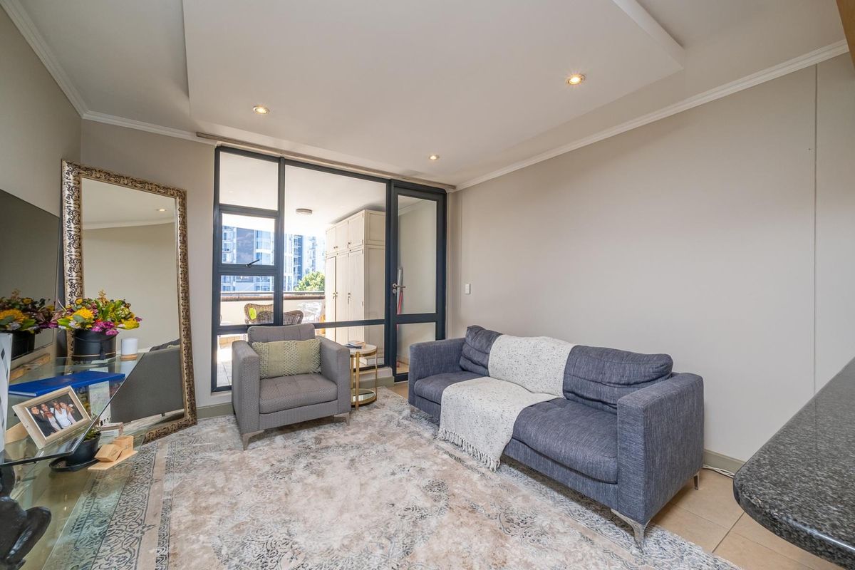 A well-lit living room featuring recessed ceiling lighting, tiled floors, and a large glass door providing access to an outdoor balcony area.