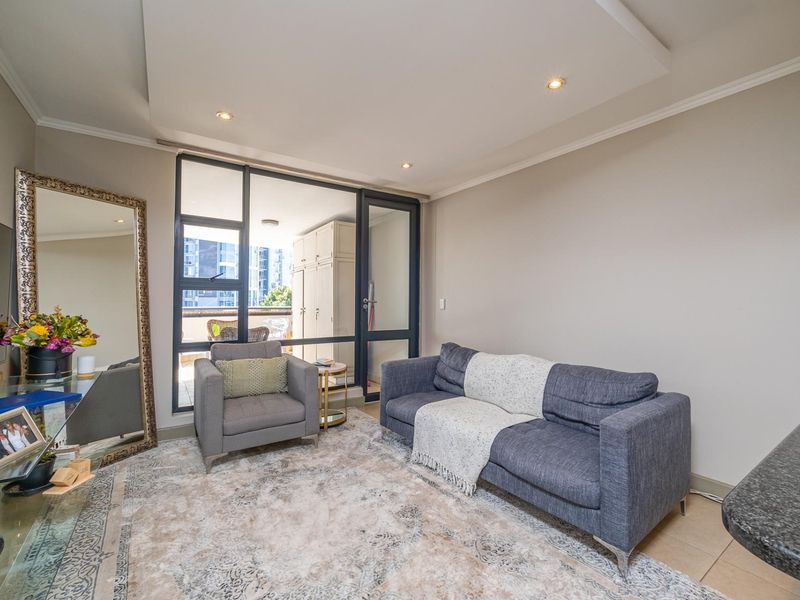 A well-lit living room featuring recessed ceiling lighting, tiled floors, and a large glass door providing access to an outdoor balcony area.
