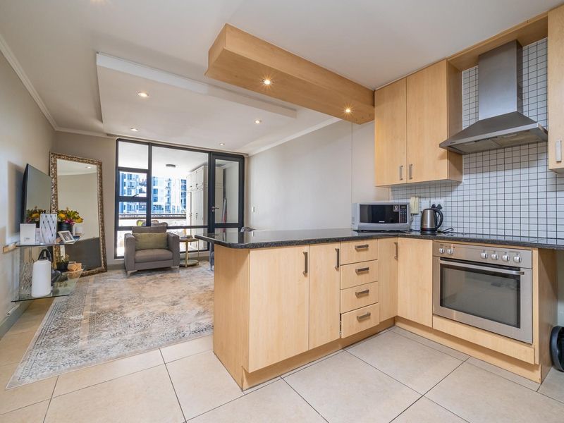 Open-plan kitchen and living area featuring light wood cabinetry, granite countertops, stainless steel appliances, and direct access to a balcony through sliding glass doors.