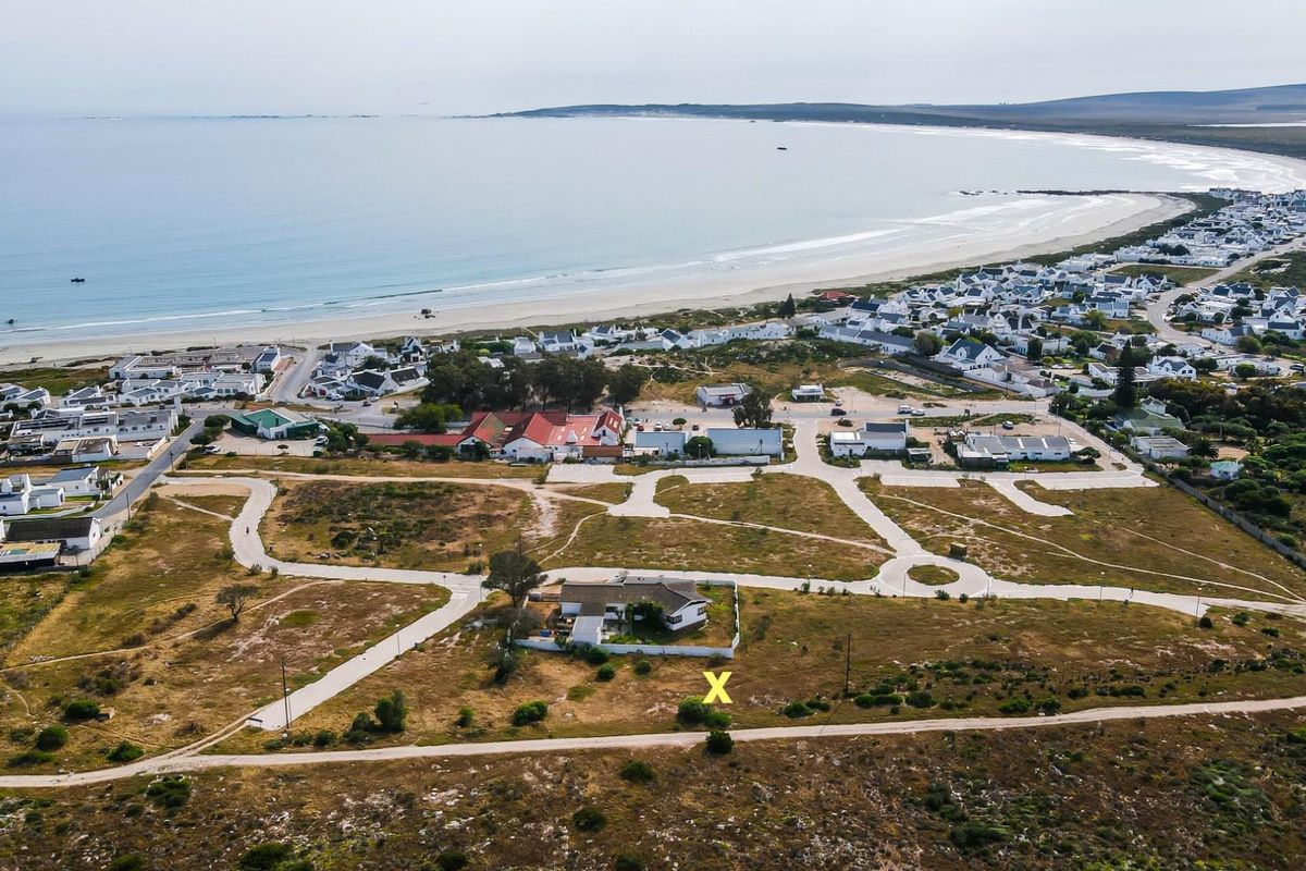 Aerial view of a residential plot marked with an X, situated in a coastal development with proximity to the beach and local infrastructure.