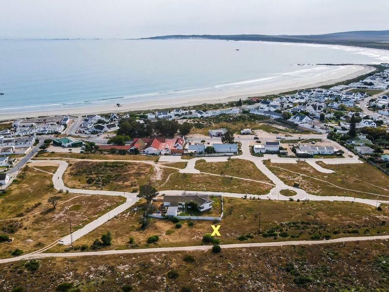 Aerial view of a residential plot marked with an X, situated in a coastal development with proximity to the beach and local infrastructure.