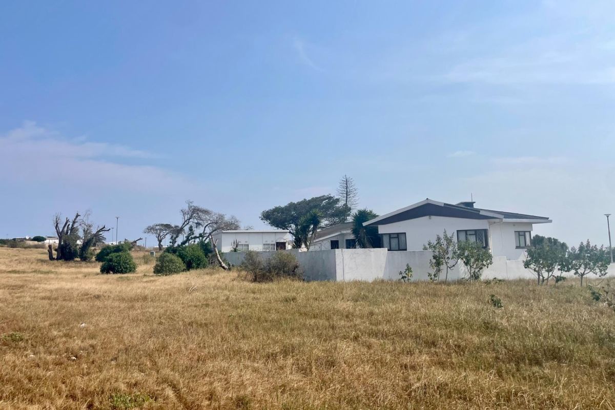 A view of the rear elevation of a residential property featuring a boundary wall and surrounding dry, unmaintained land.