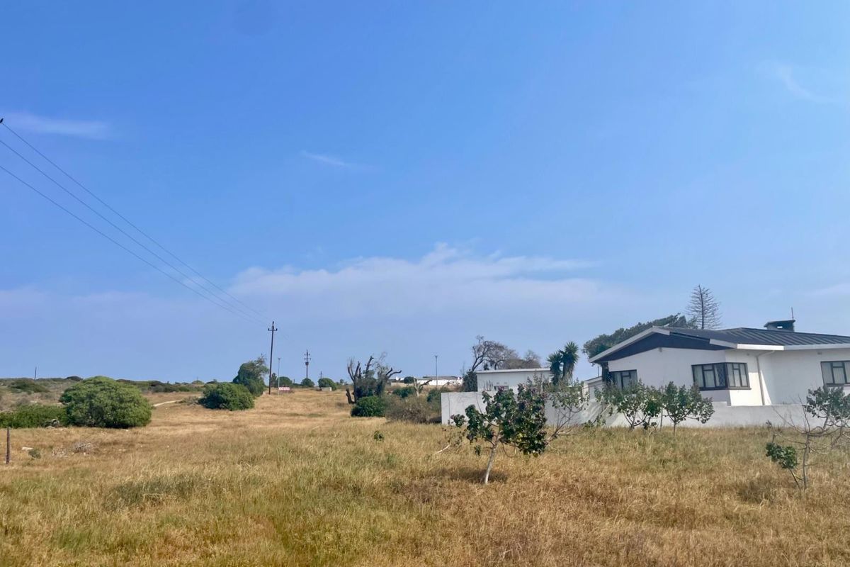 A view of a residential vacant land plot featuring dry grass, power lines, and a partial view of an adjacent white building.