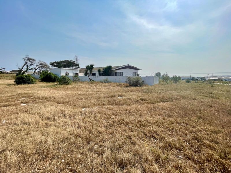 A view of a vacant residential plot featuring dry grass and a perimeter wall with security fencing.