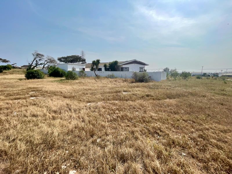 A view of a vacant residential plot featuring dry grass and a perimeter wall with security fencing.