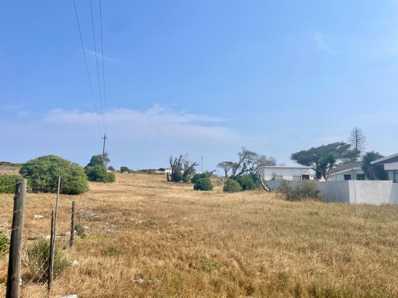 A view of a vacant residential plot featuring dry grass, perimeter fencing, and nearby utility infrastructure.