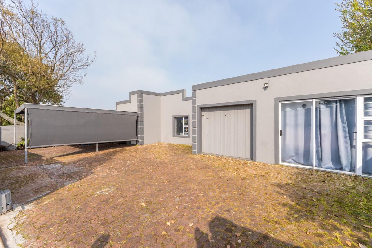 Rear exterior view featuring a paved driveway, a single garage, a sliding glass door, and a covered carport area.