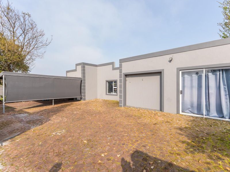 Rear exterior view featuring a paved driveway, a single garage, a sliding glass door, and a covered carport area.