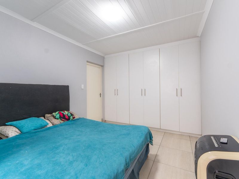 A bedroom featuring built-in cupboards, tiled flooring, and a white tongue and groove ceiling.