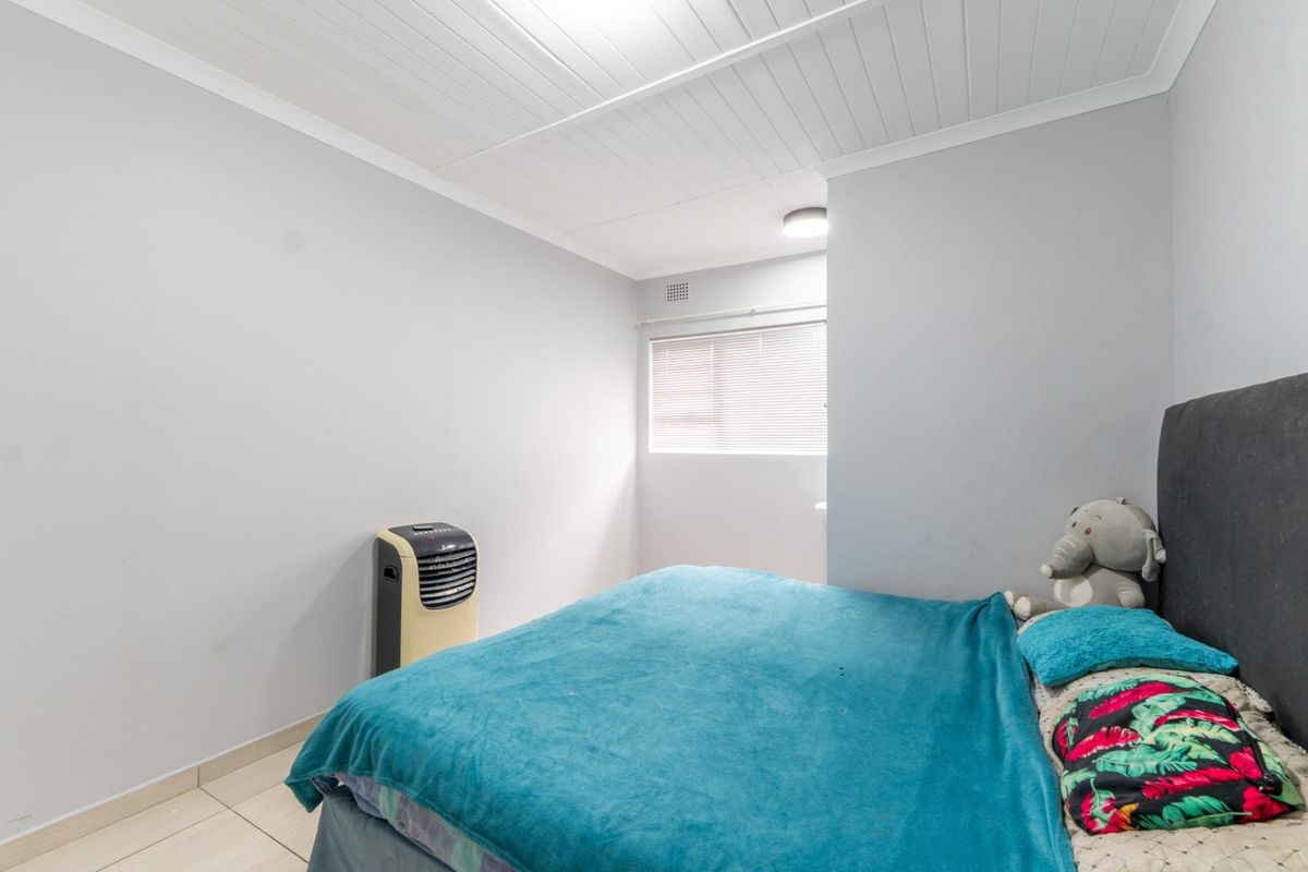A functional bedroom featuring tiled flooring, a tongue and groove ceiling, and a window fitted with venetian blinds.