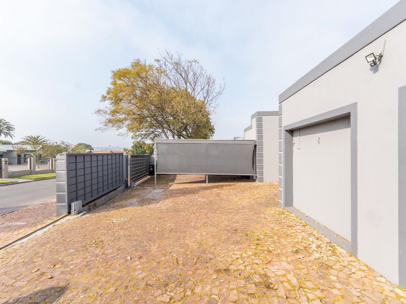 Front exterior view of the property featuring a paved driveway, garage access, and secure boundary walling with a sliding gate.