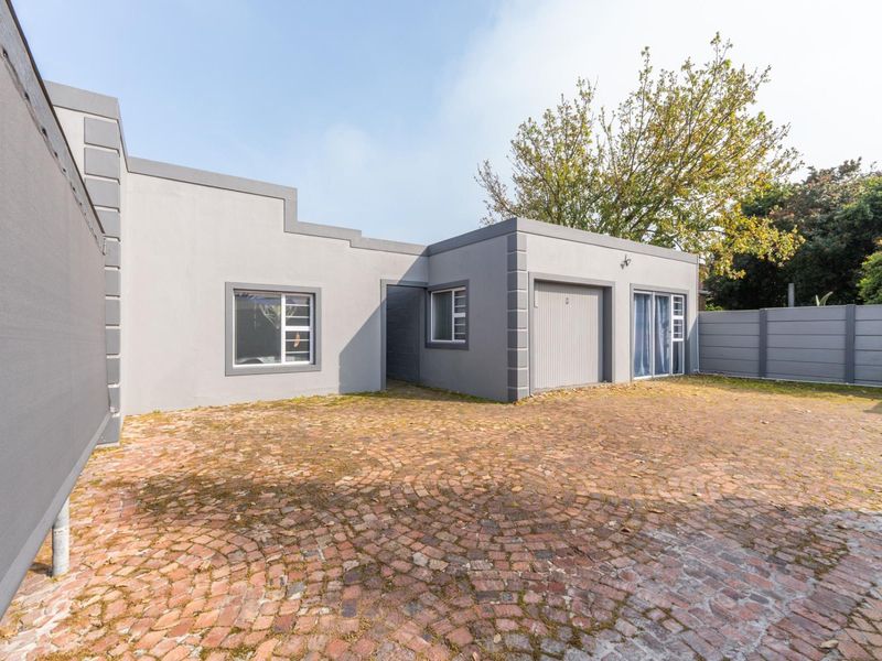 Front exterior view of the property featuring a brick paved driveway, garage access, and modern grey painted facade with aluminium window frames.