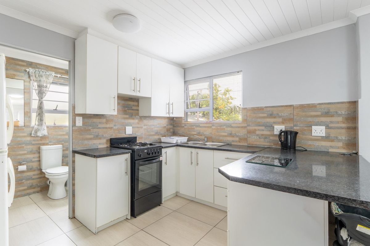 A functional kitchen featuring white cabinetry, dark countertops, tiled backsplash, and a freestanding stove, with an adjacent bathroom visible through the doorway.
