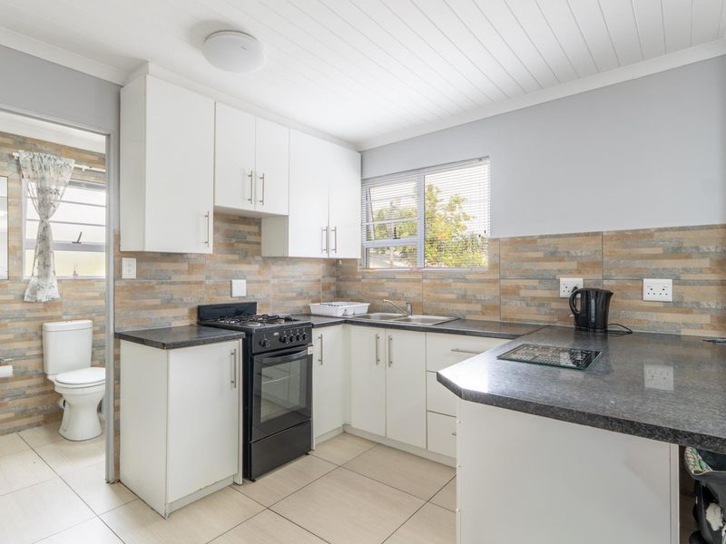 A functional kitchen featuring white cabinetry, dark countertops, tiled backsplash, and a freestanding stove, with an adjacent bathroom visible through the doorway.