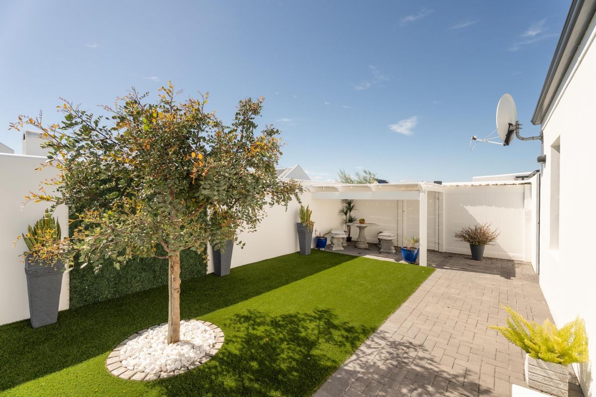 A well-maintained rear courtyard featuring a paved patio area, a pergola, and an artificial lawn with a landscaped tree.